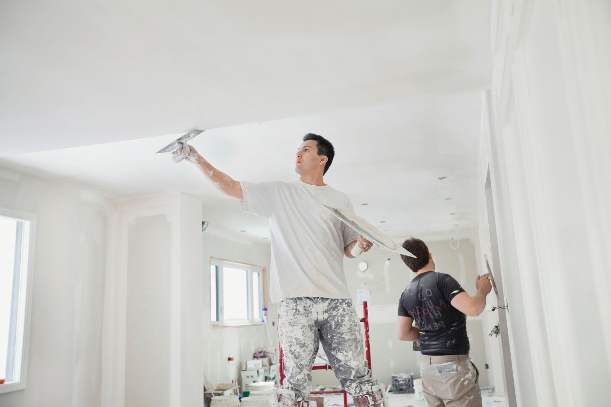 a man in a white shirt paints a white ceiling.