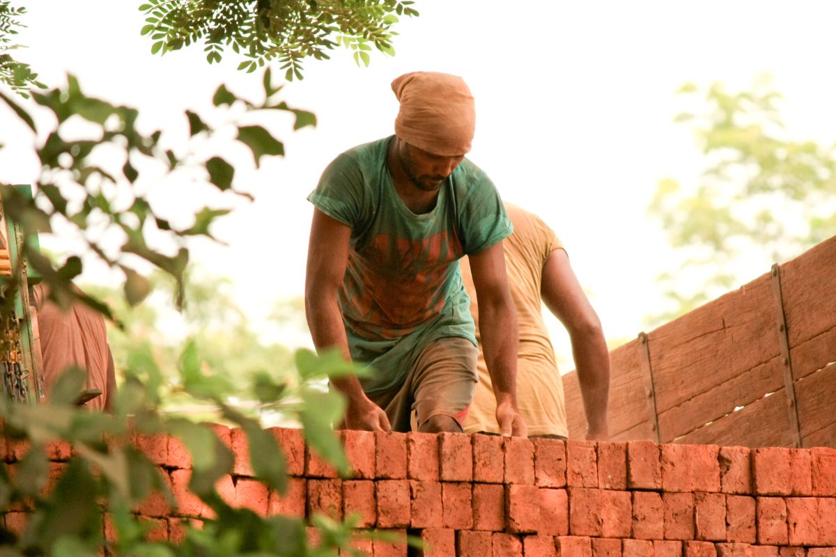 A landscaper places bricks in a yard, wearing a green shirt and bandana.