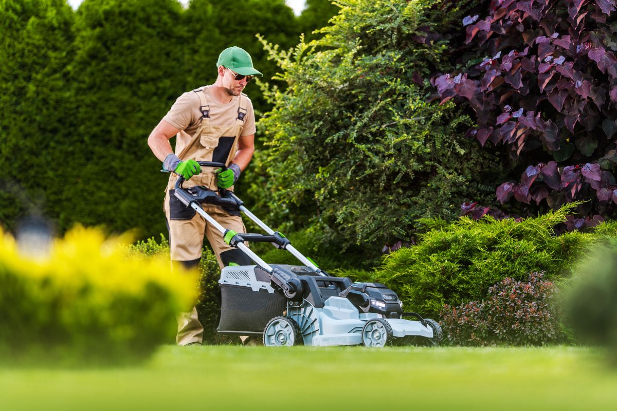 A man in brown overalls mows a yard.